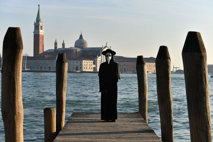 Người đàn ông hóa trang trong bộ quần áo đen và đeo mặt nạ tại Venice, phía sau là nhà thờ San Giorgio. Ảnh: AFP.
